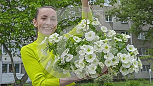 The attractive woman holding decorative petunia flower in flower pot on the street. Gardening and planting