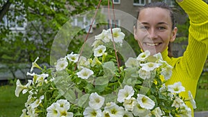 The attractive woman holding decorative petunia flower in flower pot on the street. Gardening and planting