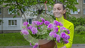 The attractive woman holding decorative petunia flower in flower pot on the street. Gardening and planting