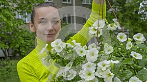 The attractive woman holding decorative petunia flower in flower pot on the street. Gardening and planting