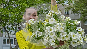 The attractive woman holding decorative petunia flower in flower pot on the street. Gardening and planting