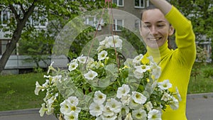 The attractive woman holding decorative petunia flower in flower pot on the street. Gardening and planting