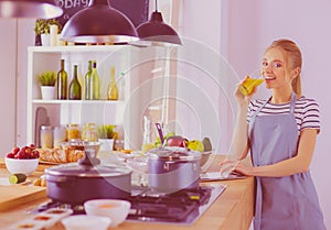 Attractive woman holding a glass of orange juice while standing in the kitchen