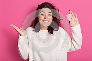 Attractive woman holding menstrual cup standing against pink background, squeesing her shoulders and spreading hand aside, looks