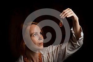 An attractive woman holds a piece of jewelry in her hand - amber pendant on a black background