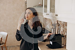 Attractive woman in the kitchen making coffee from a machine. Having breakfast in the morning