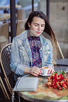 Attractive woman with long brunette hair in blue dress sitting in street cafe