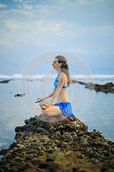 Attractive woman, meditating, practicing yoga and pranayama at the beach. Sunset yoga practice. Hands in gyan mudra. Self care