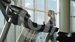Attractive woman of middle age is running on tread mill in sport gym
