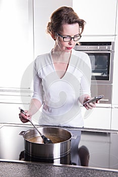 Attractive woman in modern ktchen cooking and looking on the pho