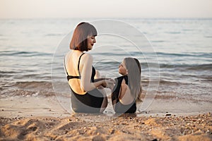 Attractive woman mother with red hair and her little cute daughter sitting on the sea beach.