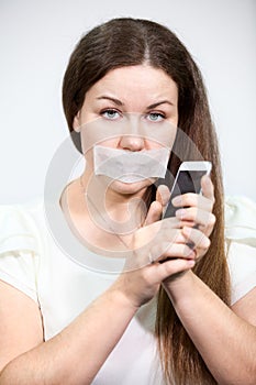Attractive woman with mouth sealed can not talk on cell phone, grey background