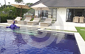 Attractive woman in a Muslim swimwear burkini enters in the pool in a tropical garden