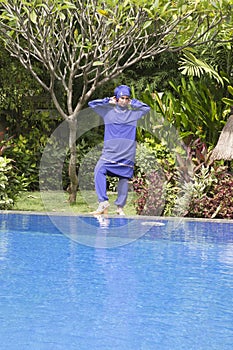 Attractive woman in a Muslim swimwear burkini stand on a pool side in a tropical garden