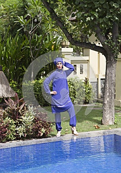 Attractive woman in a Muslim swimwear burkini stand on a pool side in a tropical garden