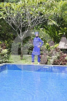 Attractive woman in a Muslim swimwear burkini stand on a pool side in a tropical garden