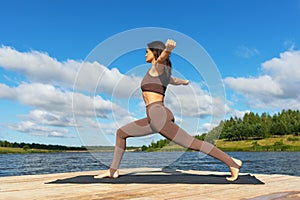 Attractive woman performing a variation of Virabhadrasana exercise, warrior pose, training in leggings and a short top