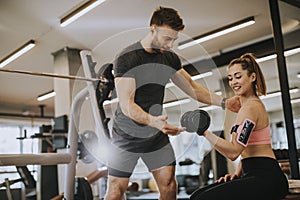 Attractive woman and a personal trainer with weight training at gym