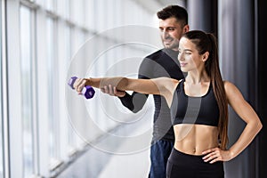 Attractive woman and a personal trainer with weight training at gym