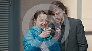 attractive woman photographer makes photo session for young handsome businessman outdoors on city street. woman showing