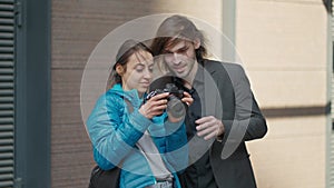 attractive woman photographer makes photo session for young handsome businessman outdoors on city street. woman showing