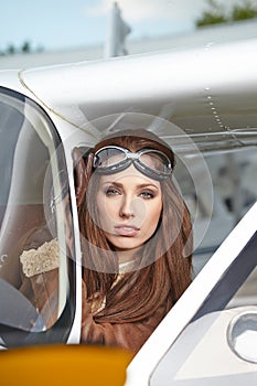 Attractive woman pilot wearing sunglasses standing in the sunshine on an airfield resting against her small private airplane