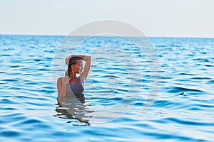 Attractive woman posing in blue sea water. Sexy female looking away with happiness. Summer holidays and vacation idea