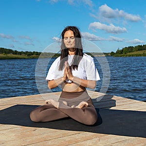 Attractive woman practicing yoga, meditating while sitting in lotus position with namaste
