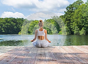 Attractive woman is practicing yoga and meditation, sitting in lotus pose near lake in morning