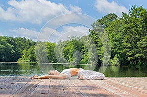 Attractive woman is practicing yoga and meditation in Supta Virasana pose near lake in morning