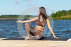 An attractive woman practicing yoga relaxes after a workout while sitting on the shore of a lake, shows the mudra symbol, works