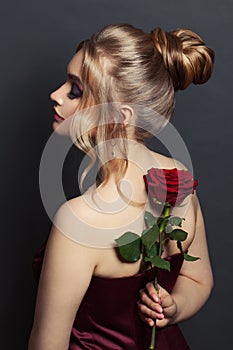 Attractive woman profile and back head with blonde hair updo hairdo and red rose flower on black