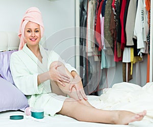 Attractive woman putting cream on legs