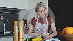 Attractive woman is reading a book while cooking dinner. Pleased young woman laughs while reading a novel. Home