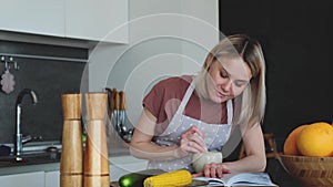 Attractive woman is reading a book while cooking dinner. Pleased young woman laughs while reading a novel. Home