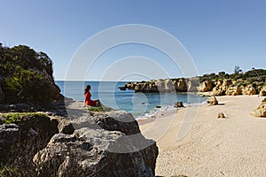 Attractive woman in red dress on top of cliffs at Sao Rafael Beach, Algarve, south Portugal