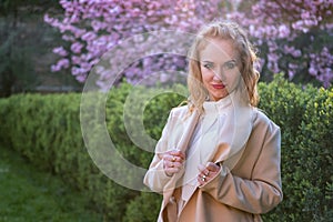 Attractive woman with red hair stare in camera in blooming spring park on cherry blossom tree background. Portrait