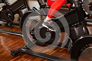 Attractive woman in a red sports suit in gym, riding on speed stationary bike. Women`s legs close up