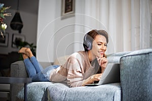 Attractive woman relaxing at home and using earphone and laptop