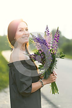 Attractive woman on the road in a summer field among Lupinus flowers.