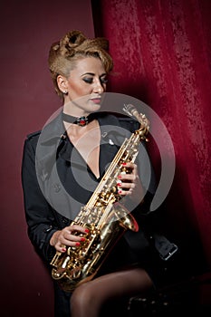 attractive woman with saxophone posing on red background. Young sensual blonde playing sax. Musical instrument, jazz