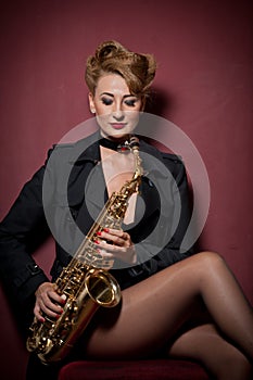 attractive woman with saxophone posing on red background. Young sensual blonde playing sax. Musical instrument, jazz