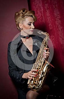 attractive woman with saxophone posing on red background. Young sensual blonde playing sax. Musical instrument, jazz