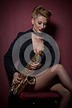 attractive woman with saxophone posing on red background. Young sensual blonde playing sax. Musical instrument, jazz