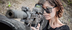 Attractive woman shooting with rifle machine gun from behind barricade