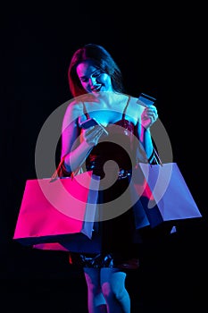Attractive woman with shopping bags typing credit card number in smartphone app, online payments. Isolated on black
