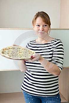 Attractive woman showing big tasty pizza while standing in domestic room