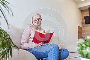 Attractive woman sitting on bed in the morning, drinking tea, reading book, casual style, blue jeans, pink sweater, feeling