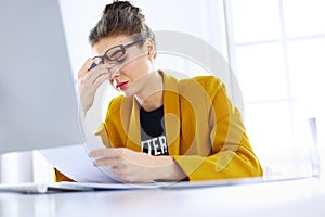 Attractive woman sitting at desk in office, working with laptop computer, holding document