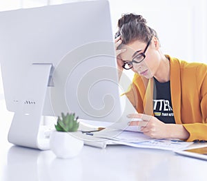 Attractive woman sitting at desk in office, working with laptop computer, holding document